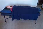 Reiki client lies on massage table with a blanket over her arms, legs and torso.