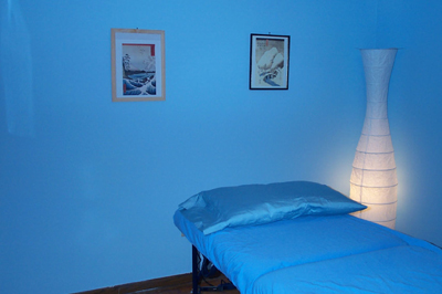 Reiki treatment and attunement room with sky blue walls, framed prints, a massage table with sky blue linens and a soft rice paper lamp.